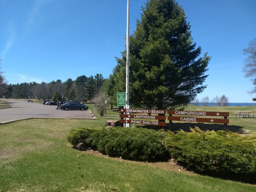 Signpost directing to beach, campground, lighthouse, picnic shelter, and cabins, with a clear blue sky and green grass.