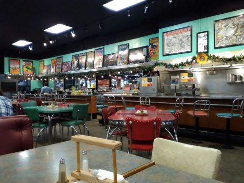A retro diner interior with colorful seating, a long counter, and walls adorned with vintage posters and holiday decorations.
