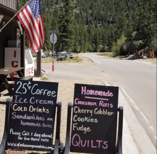 A roadside store with signs for coffee, ice cream, and homemade treats, alongside an American flag and a scenic backdrop.