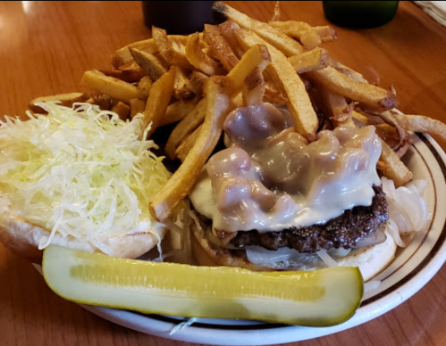 A plate featuring a burger with melted cheese and toppings, served with a side of crispy French fries and a pickle.