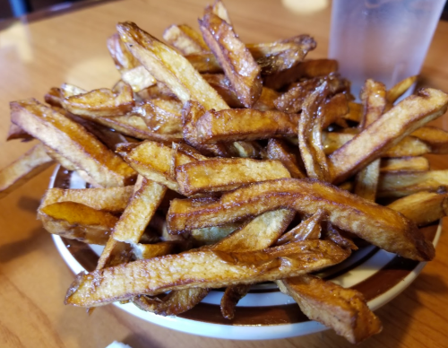 A heaping bowl of golden-brown French fries on a wooden table.