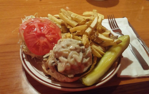A plate with a burger topped with sauce, lettuce, tomato, a side of fries, and a pickle.