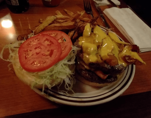 A juicy burger with melted cheese, bacon, lettuce, and tomato, served with a side of crispy fries on a plate.