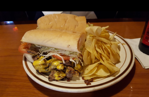 A plate with two sandwiches filled with meat, cheese, and vegetables, accompanied by a side of potato chips.