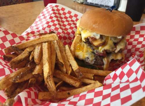 A juicy burger with melted cheese and toppings, served with a side of crispy French fries in a red-checkered basket.