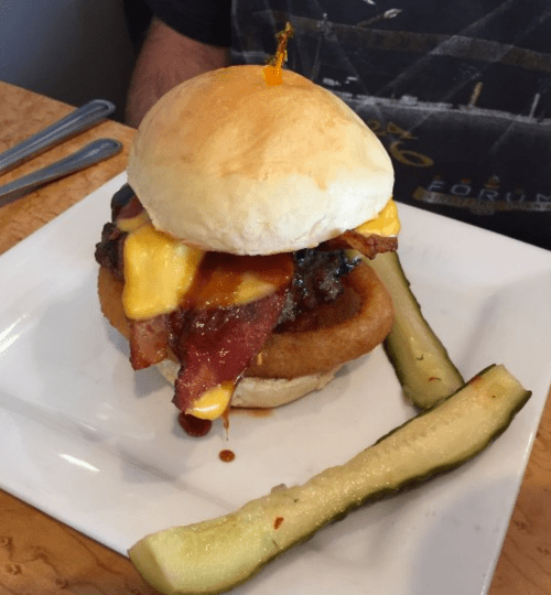 A juicy burger topped with cheese, bacon, and barbecue sauce, served with pickles on the side.