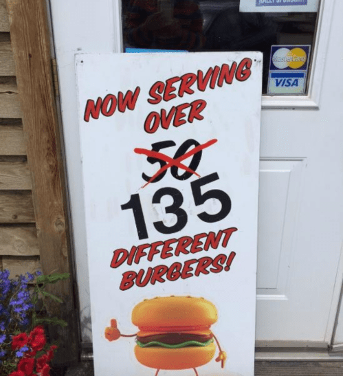 Sign outside a restaurant announcing "Now serving over 135 different burgers!" with a cartoon burger graphic.