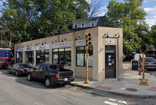 A street view of a small commercial building with multiple storefronts and parked cars nearby.