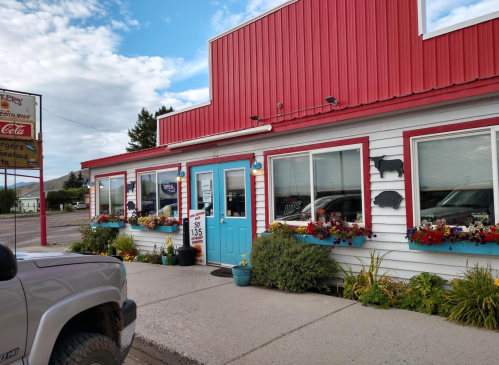A colorful restaurant with a red roof, blue door, and flower boxes, featuring a sign and a parked truck in front.