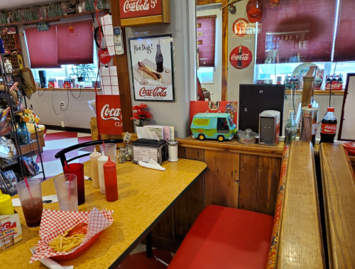 A cozy diner table with fries, condiments, and a toy truck, surrounded by Coca-Cola memorabilia and a vibrant decor.