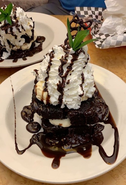A towering dessert of brownies, vanilla ice cream, whipped cream, and chocolate sauce, garnished with a mint leaf.