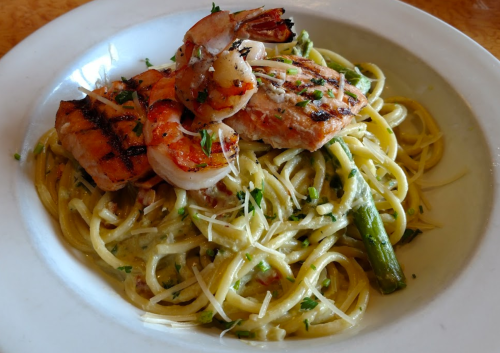 A plate of linguine topped with grilled shrimp, asparagus, and a creamy sauce, garnished with parsley.