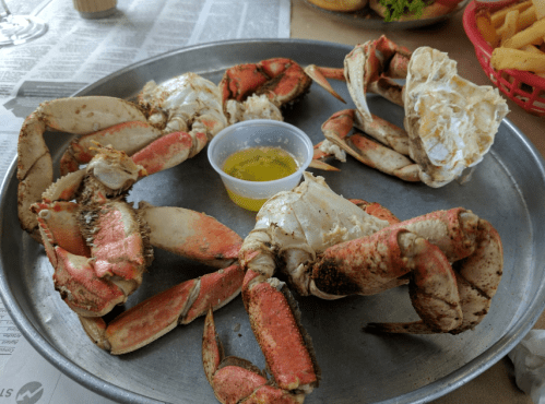 A metal platter with several cooked crabs and a small cup of melted butter for dipping.