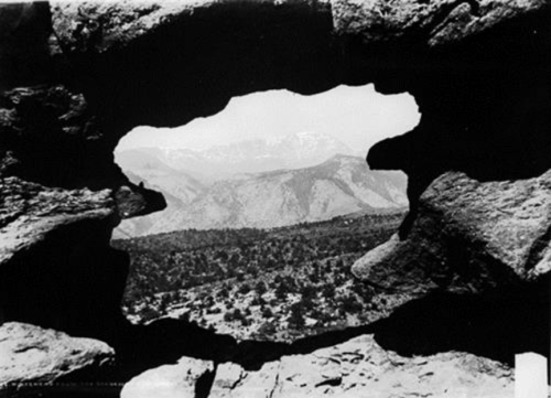A view of mountains through a natural rock formation, showcasing a rugged landscape in black and white.