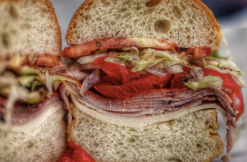 Close-up of a sandwich with layers of deli meats, lettuce, and tomato between two slices of bread.
