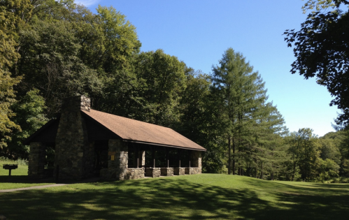 A stone pavilion surrounded by lush green trees under a clear blue sky.