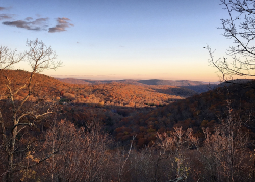 A scenic view of rolling hills covered in autumn foliage under a clear sky at sunset.