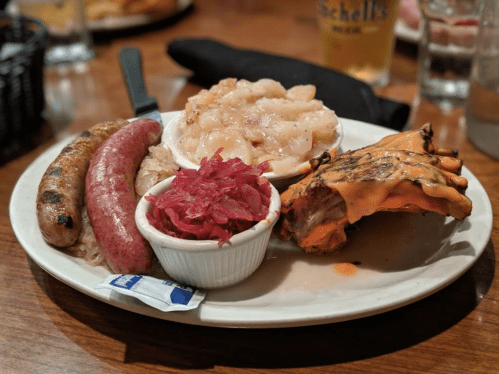 A plate of assorted meats including sausages, chicken, sauerkraut, and red cabbage, served with a side of mashed potatoes.