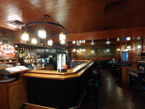 A cozy bar interior with wooden decor, a well-stocked bar, and a few patrons seated at tables.