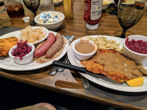 Two plates of food featuring meats, sides of sauerkraut, mashed potatoes, and gravy, served on a wooden table.