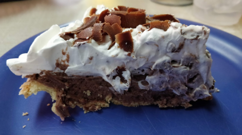 A slice of chocolate cream pie topped with whipped cream and chocolate shavings on a blue plate.