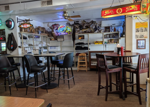Interior of a rustic restaurant with wooden floors, tables, and shelves displaying memorabilia and decor.