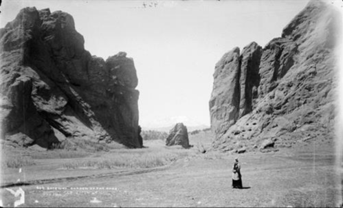 A person stands in a vast canyon surrounded by towering rock formations under a clear sky.