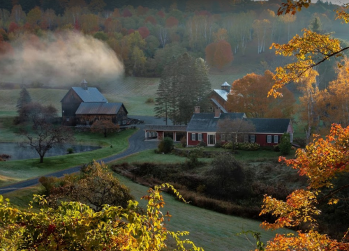 A serene autumn landscape featuring a farmhouse and barn surrounded by colorful trees and misty hills.