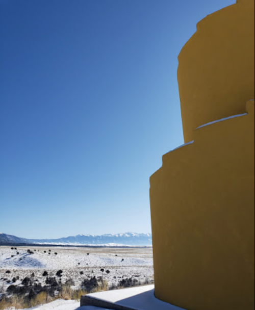 A yellow structure in the foreground with a snowy landscape and mountains under a clear blue sky in the background.