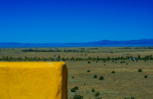 A vast landscape with rolling hills and distant mountains under a clear blue sky, viewed from a yellow wall.