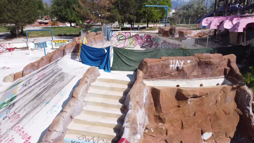 An abandoned skate park with graffiti, featuring rock-like structures and a makeshift tent.