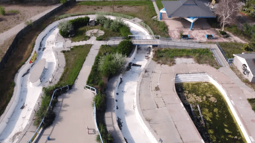 Aerial view of an abandoned water park with overgrown paths and a dilapidated building in the background.