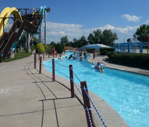 A water park scene featuring a lazy river, water slides, and people enjoying the sunny day.