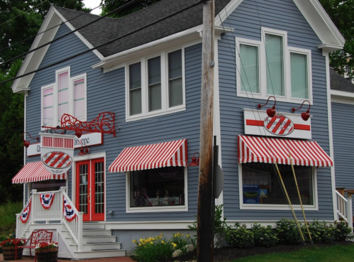 A charming blue house with red and white striped awnings, featuring a candy shop entrance and decorative cherry accents.