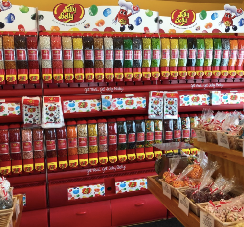 A colorful display of Jelly Belly jelly beans in various flavors, arranged in clear containers on shelves.