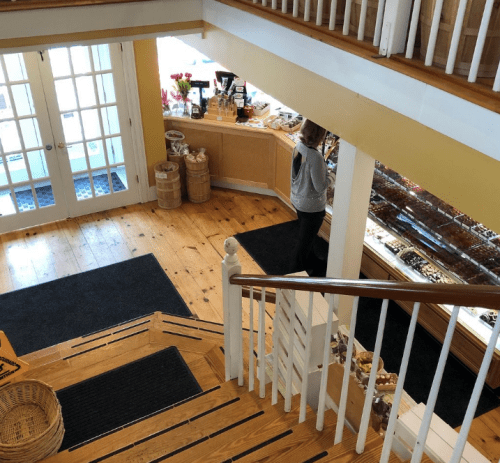 A cozy shop interior with wooden floors, a staircase, and a customer browsing a display of treats.