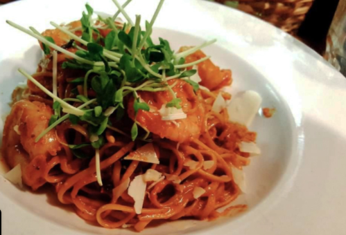 A plate of noodles topped with shrimp, green onions, and herbs, garnished with shredded cheese.