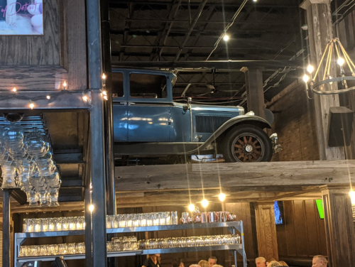 A vintage car displayed on a wooden shelf in a rustic restaurant, with glassware and dim lighting in the foreground.
