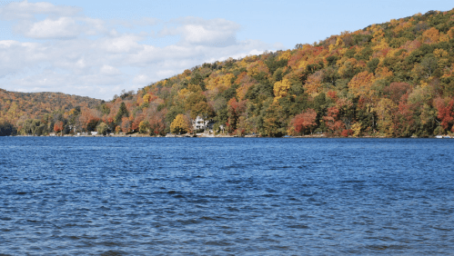 A serene lake surrounded by vibrant autumn foliage on rolling hills under a partly cloudy sky.