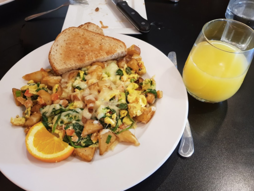 A plate of scrambled eggs with vegetables and potatoes, served with toast and a glass of orange juice.