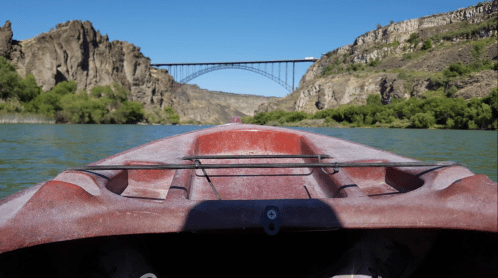 View from a kayak on a river, with a bridge spanning rocky cliffs in the background under a clear blue sky.