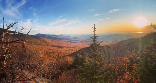 A panoramic view of a colorful autumn landscape with mountains and a sunset in the background.