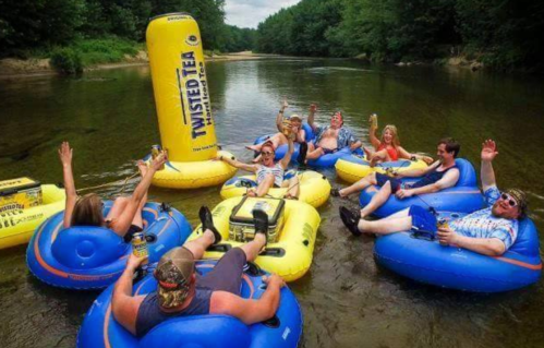 A group of people enjoying a summer day floating on inner tubes in a river, waving and relaxing with drinks.