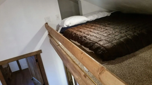 Cozy loft bedroom with a wooden railing, featuring a bed covered in a dark quilt and two pillows.