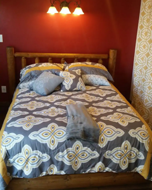 A cozy bedroom with a wooden bed, patterned bedding, and warm red walls, featuring two wall sconces.
