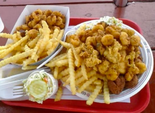 A tray of crispy fried seafood, including shrimp and calamari, served with crinkle-cut fries and a side salad.