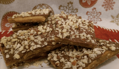 A plate of chocolate-covered toffee bark topped with chopped nuts, set against a festive background.