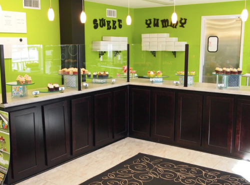 Brightly colored dessert shop interior with a counter displaying cupcakes and a green accent wall.