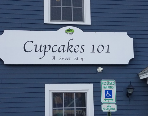 Sign for "Cupcakes 101" sweet shop on a blue building, with reserved parking signs nearby.