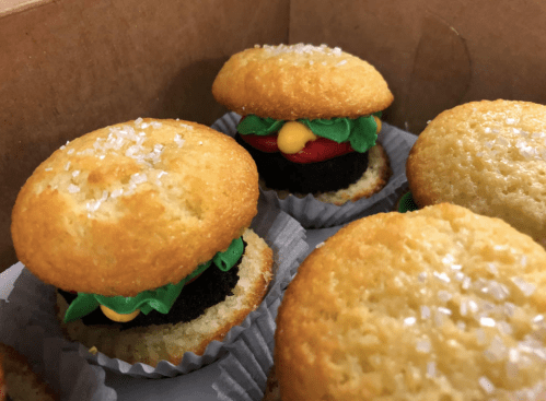 A box of mini cupcake burgers, featuring yellow frosting for cheese, red for ketchup, and green for lettuce.